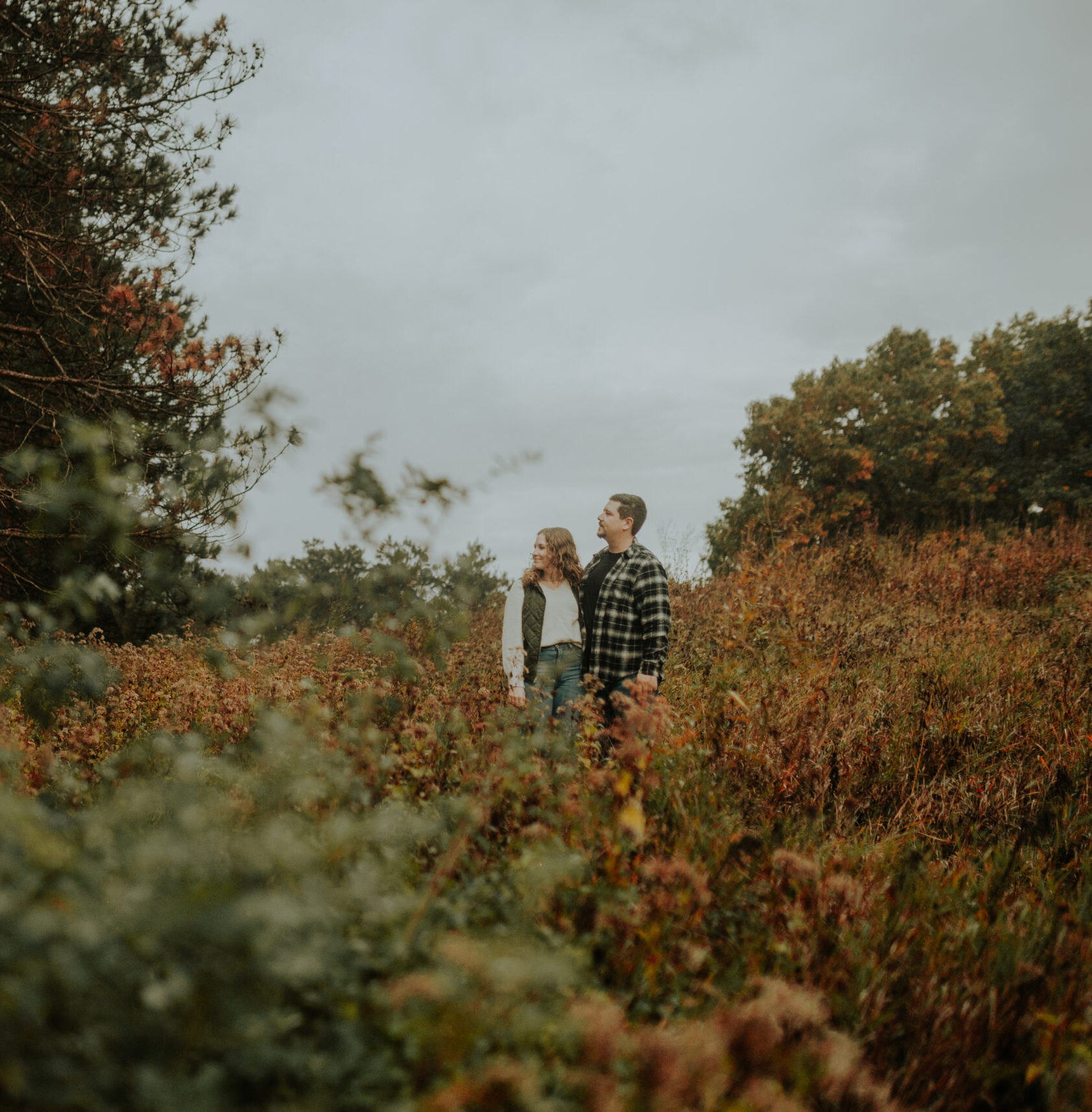 Andi and Clay sharing cozy glances at Veterans Acres on a chilly, rainy October day, surrounded by vibrant fall leaves.