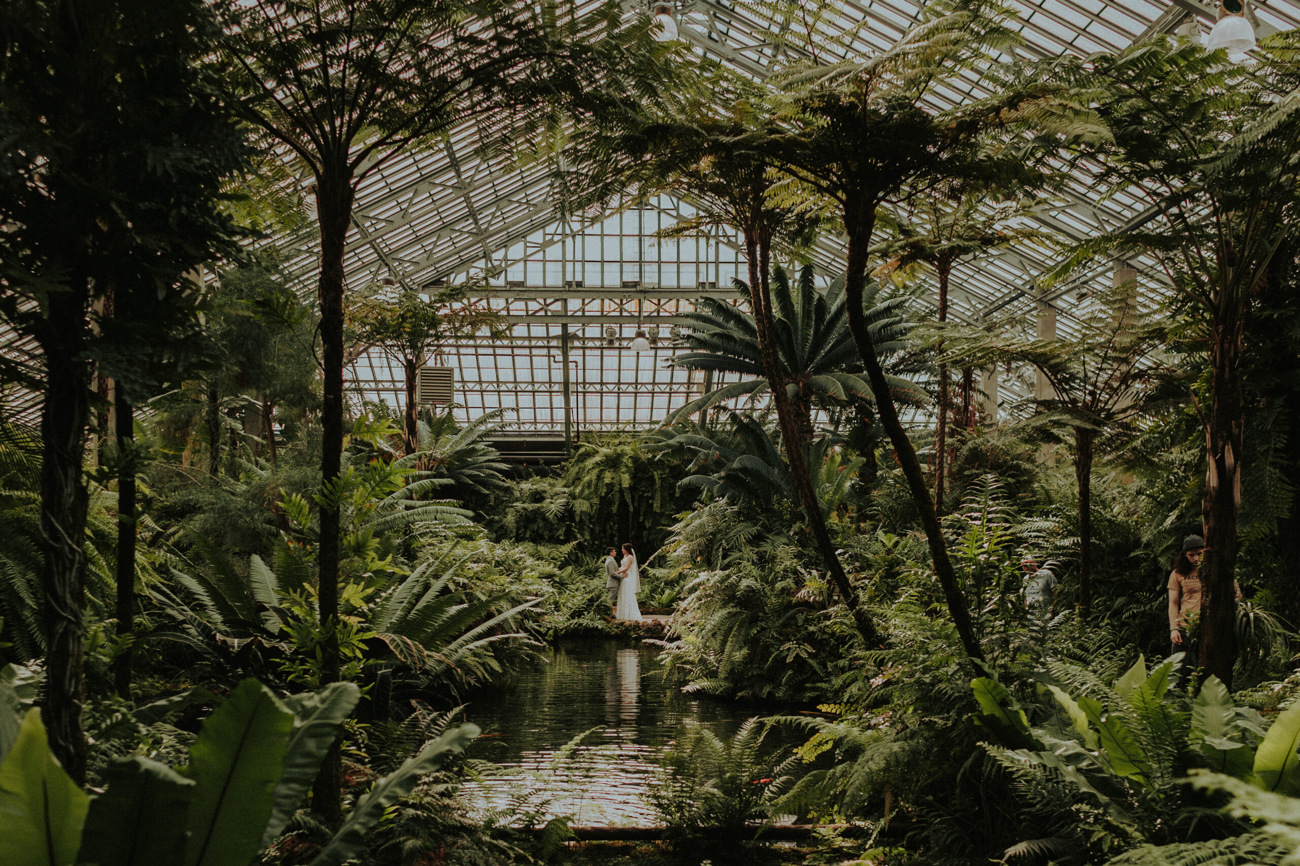 Bride and groom share a joyful kiss surrounded by lush greenery at Garfield Park Conservatory in Chicago, celebrating their wedding with friends and family from around the world