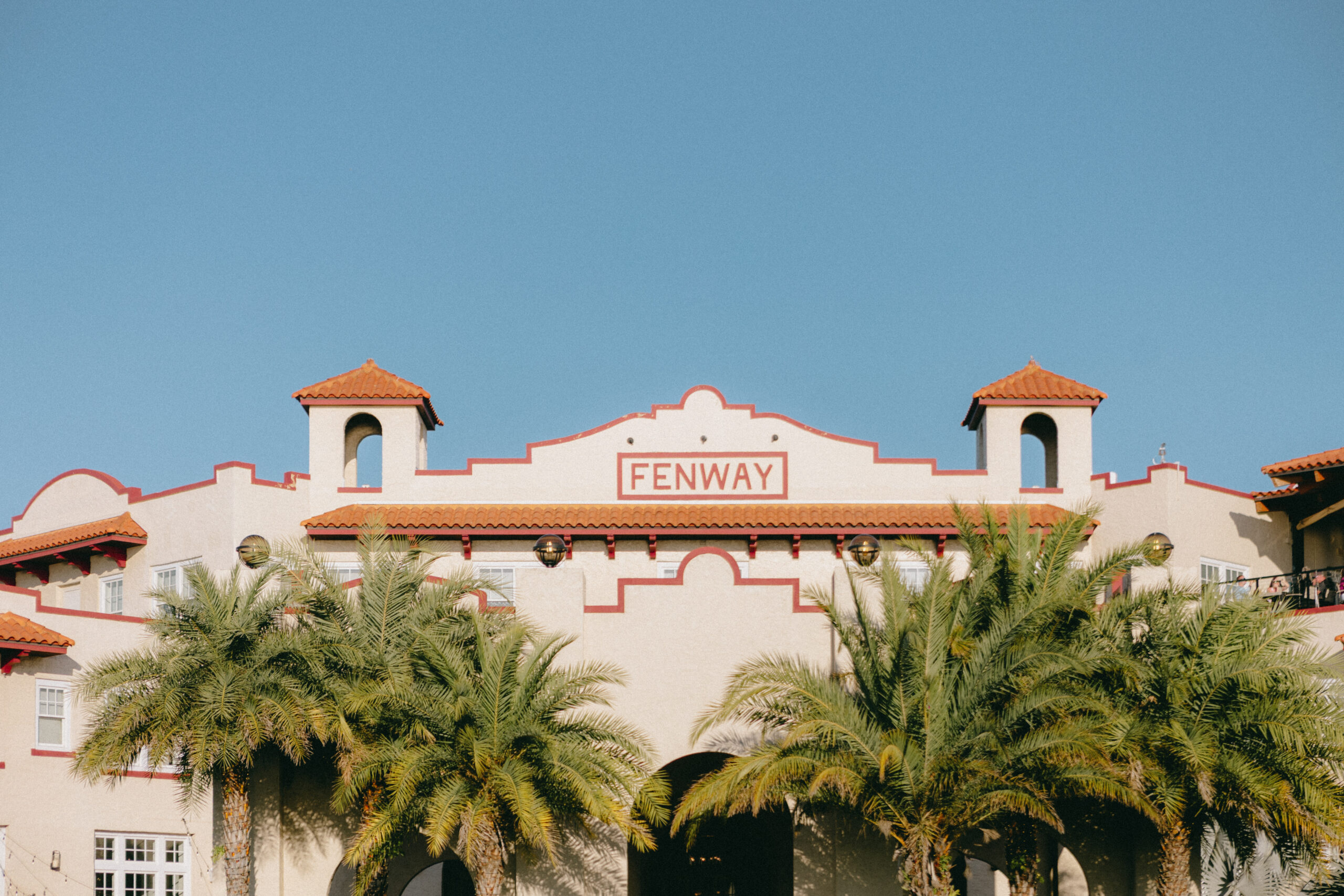 Fenway Hotel facade in Dunedin Florida with terracotta roof tiles and palm trees against a clear blue sky