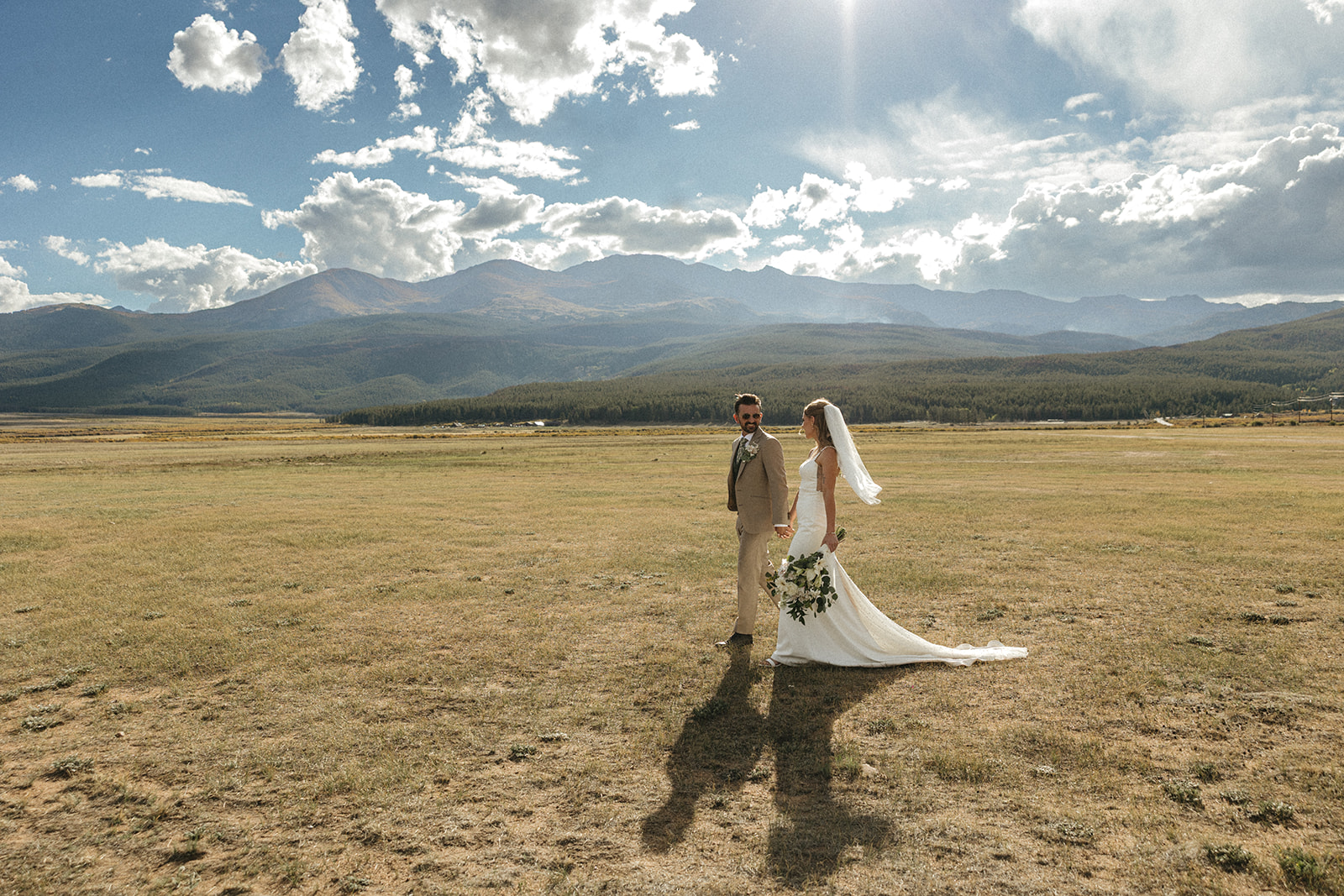 Newlyweds take a stroll in a field at the base of the mountain range in Leadville Colorado